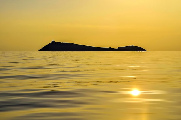 Isla con faro en medio del mar al amanecer con el reflejo del sol en el agua