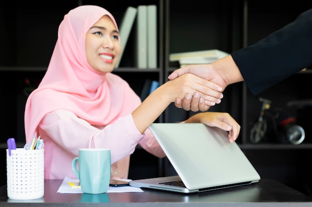 Islã muçulmano negócios handshaking. camisa de mulher muçulmana asiática rosa. mão de mulheres de negócios com papel escrito no gráfico.