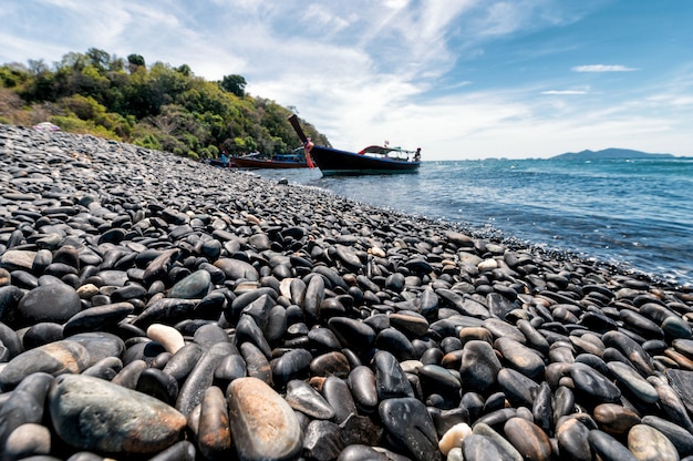 Isla de piedra negra con barco de madera en la costa en el mar tropical