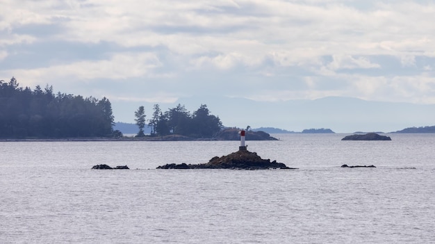 Isla rocosa con faro, océano e islas circundantes con árboles en un día nublado