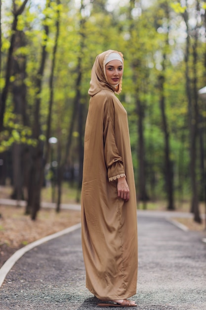 Islamische schöne Frau in einem muslimischen Kleid, das auf einem Sommerparkstraßenhintergrundwald-Herbstbäumen steht