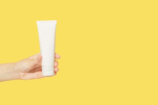 Isolado de creme para mãos e unhas em um recipiente de plástico branco em uma mão feminina em um fundo amarelo. Loção para o corpo. Cosméticos de beleza de embalagens vazias simples. Zombe, copie o espaço.