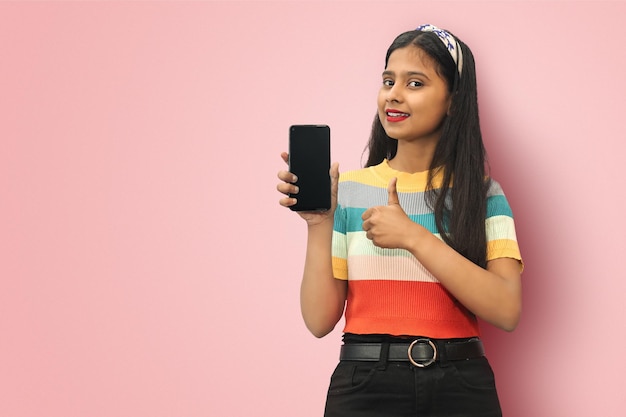Isoliert Porträt eines lächelnden, fröhlichen jungen indischen asiatischen Mädchens, das einen leeren Smartphone-Bildschirm hält und den Daumen mit Kopierraum zeigt