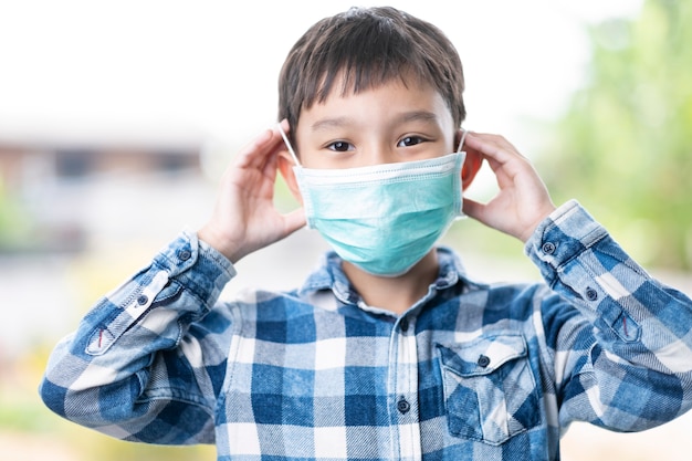 Isolierte asiatische Kinderjungenkinder, die eine grüne Maske aufsetzen, die Gesicht, Nase, Mund, Konzept des Schutzes vor Koronaviruskrankheit, Keimen und luftgeborener Übertragung korrekt bedeckt