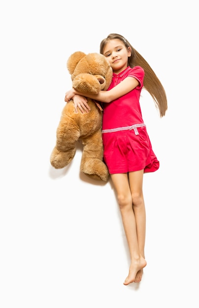 Isolierte Aufnahme von der Spitze eines süßen Mädchens, das auf dem Boden liegt und einen großen Teddybären umarmt