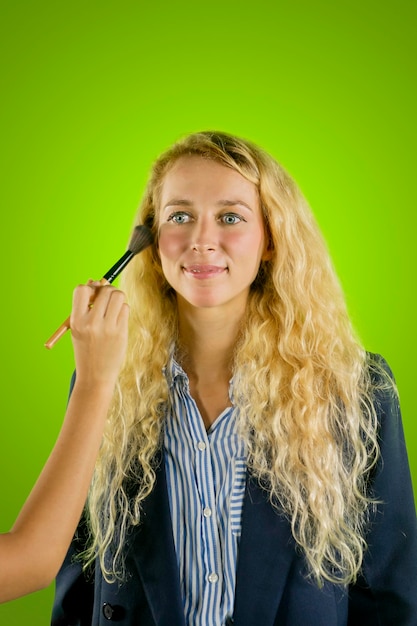 Isolierte schöne kaukasische Frau mit Make-up-Pinsel auf grünem Hintergrund