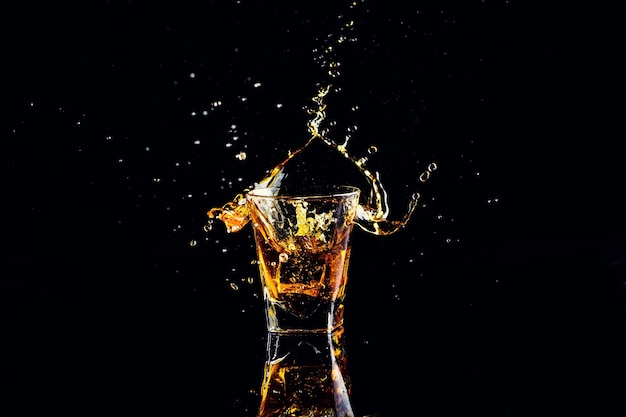 Isolierte Schuss Whisky mit Splash auf schwarzem Hintergrund Brandy in einem Glas