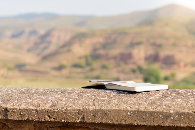 Isoliertes offenes Notizbuch mit hinterem Stift darauf, das sich auf den Boden lehnt, mit wunderschönen Landschaftsansichten im Hintergrund