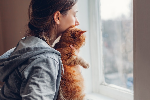 Isolierung zu hause während der coronavirus-covid-19-pandemie. frau, die fenster mit katze betrachtet.