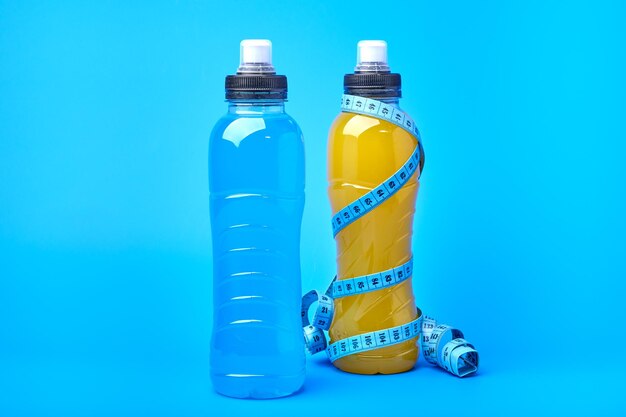 Isotonisches Energie-orange-gelbes und blaues Sportgetränk in Plastikflaschen und Maßband auf Blau