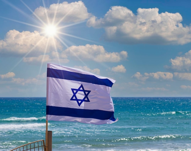 Israelische Flagge in der Sonne mit bewölktem Himmel und Meer im Hintergrund Das Konzept des israelischen Unabhängigkeitstages Yom Haatzmaut Flagge Israel mit Mast weht im Wind Nationale Staatssymbole kopieren Raum