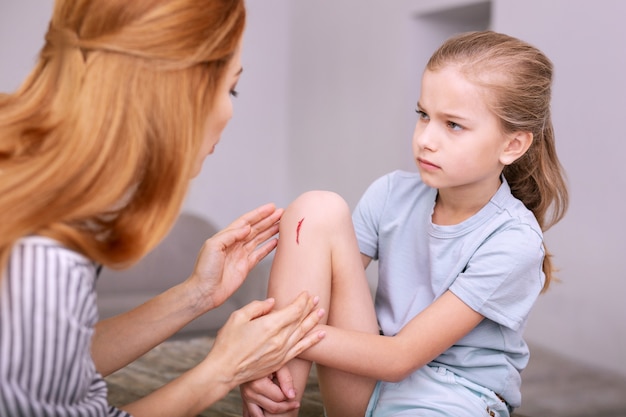 Isso dói. Menina triste e triste olhando para a mãe enquanto mostra a ela