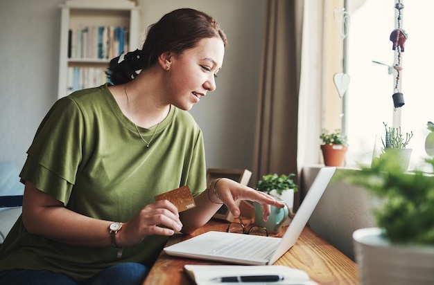 Isso é exatamente o que eu preciso Foto recortada de uma jovem empresária atraente sentada sozinha em seu escritório em casa e usando seu laptop para fazer compras on-line