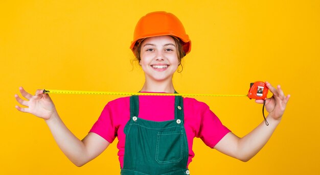 Isso vai ser perfeito. criança usar capacete no canteiro de obras. construtor de menina adolescente com fita métrica de ferramenta de construção. criança no trabalho de reparação. conceito de renovação na oficina. carpinteiro profissional ocupado.