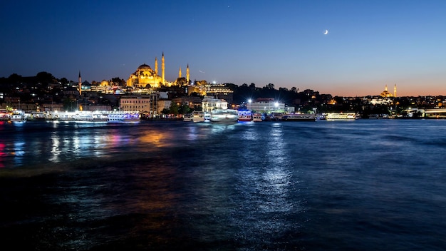 Istanbul-Stadtbild mit Süleymaniye-Moschee mit touristischen Schiffen, die nachts am Bosporus schwimmen