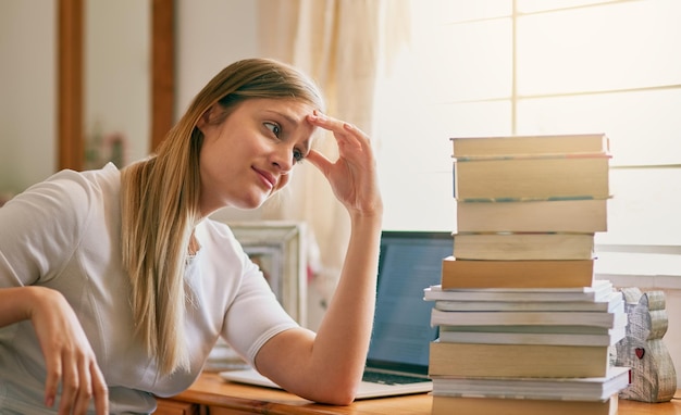 Isto é o que recebo por procrastinar Foto de uma jovem parecendo sobrecarregada com a pilha de livros em sua mesa