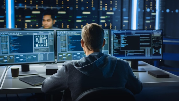 IT-Spezialist arbeitet auf Personalcomputer mit Bildschirmen, die Software-Programme mit Codierungssprache-Schnittstelle im Hintergrund des technischen Raumes des Rechenzentrums mit professionellem Arbeitsumfeld anzeigen