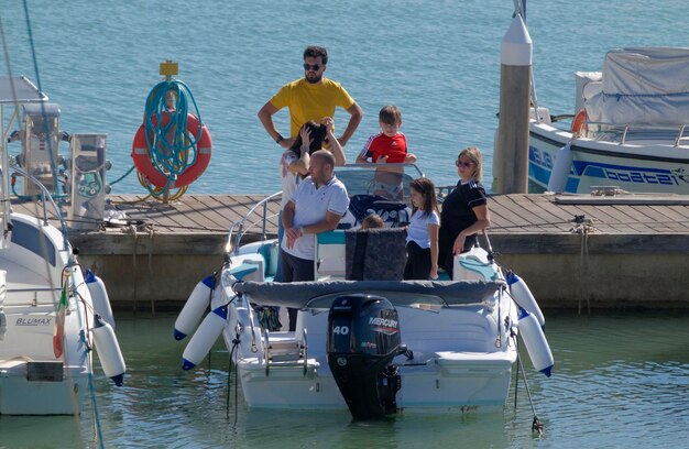 Foto italia, sicilia, mar mediterráneo, marina di ragusa (provincia de ragusa); 29 de octubre de 2023, personas en un barco a motor en el puerto - editorial