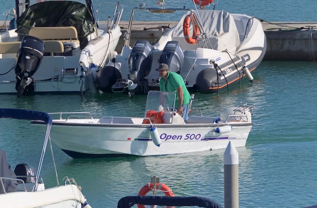 Foto italia, sicilia, mar mediterráneo, marina di ragusa (provincia de ragusa); 31 de octubre de 2020, pescador en un barco a motor en el puerto - editorial