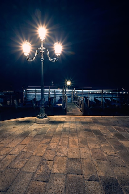 Italia, terraplén de Venecia en la noche. Farola histórica con goldolas y San Giorgio di Maggiore. Imagen de fondo de viajes monocromática.