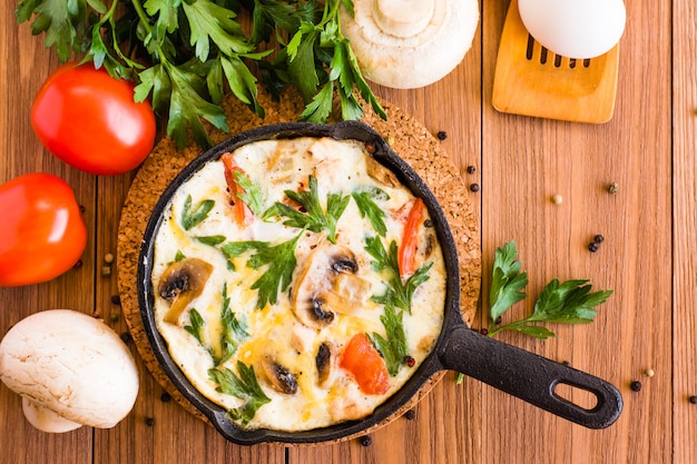 Italiener Frittata, Tomaten, Pilze und Petersilie auf einem Holztisch. Ansicht von oben