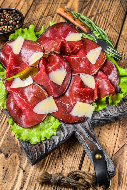 Italienische Antipasti Bresaola-Fleisch mit grünem Salat und Parmesan. hölzerner Hintergrund. Ansicht von oben.