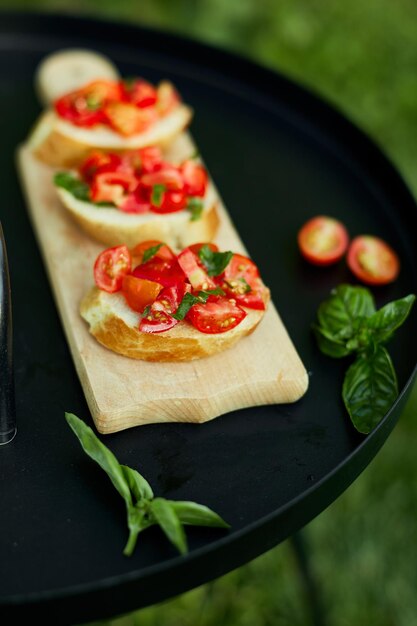 Italienische Bruschetta mit frischen roten Tomaten und Basilikumkräutern auf einem Holzbrett im Freien