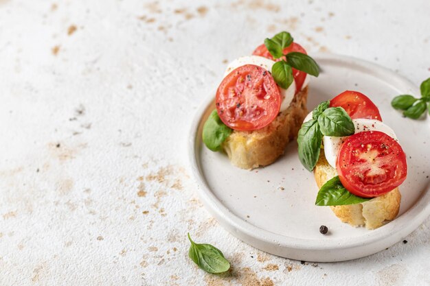 Italienische Bruschetta mit Tomaten, Mozzarella und Basilikum auf weißer Platte mit Textraum