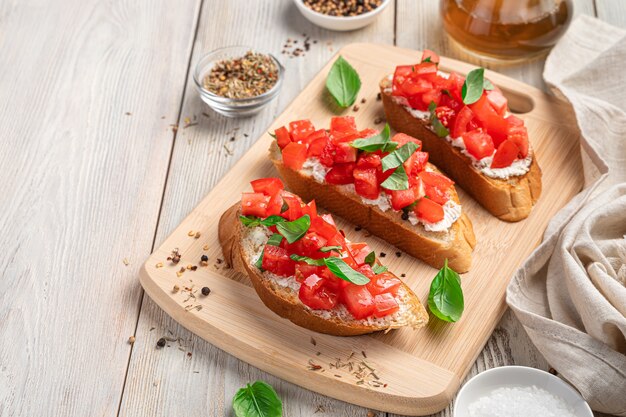 Italienische Bruschetta mit Tomaten, Weichkäse und Basilikum auf beigem Holzhintergrund. Seitenansicht, Kopienraum.