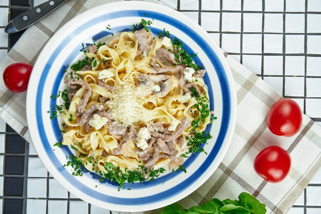 Italienische Fettuccine-Nudeln in Käsesauce mit Parmesan, Huhn und Schinken, Kräuter in weißer Keramikschale auf weißer Oberfläche.