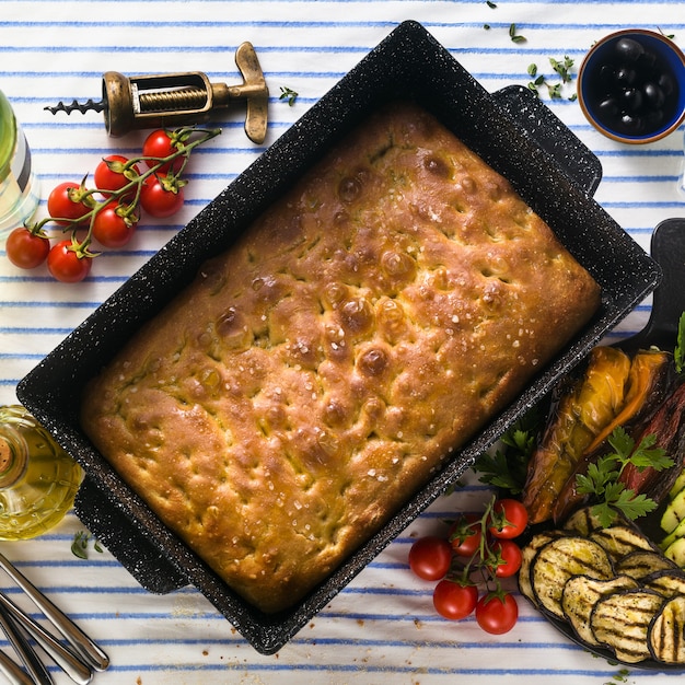 Italienische Focaccia und gegrilltes Gemüse auf einem Tisch mit Rotwein und aromatischen Kräutern. Sommermenü