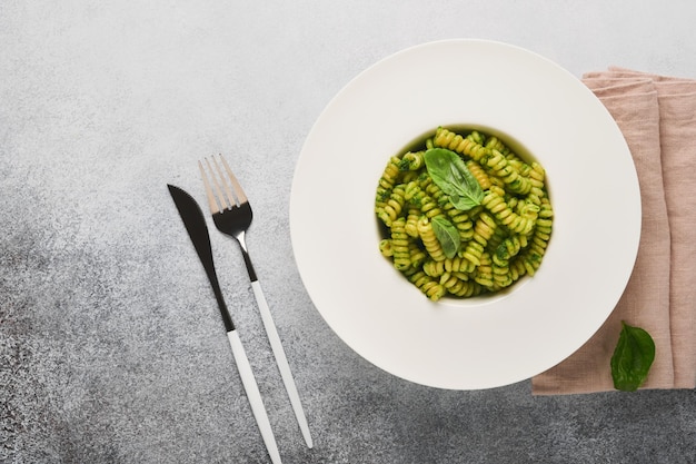 Italienische Fusilli-Nudeln mit Pesto Fusilli-Nudeln mit Basilikum-Pesto und Kräutern Parmesan-Käse-Basilikum und Knoblauch auf weißem Teller auf grauem Stein-Arbeitsplattenhintergrund Draufsicht Kopierbereich Mock-up