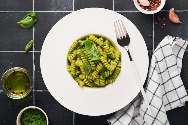 Italienische Fusilli-Nudeln mit Pesto Fusilli-Nudeln mit Basilikum-Pesto und Kräutern Parmesan-Käse-Basilikum und Knoblauch auf weißem Teller auf schwarzem Stein-Arbeitsplattenhintergrund Draufsicht Kopierbereich Mock-up