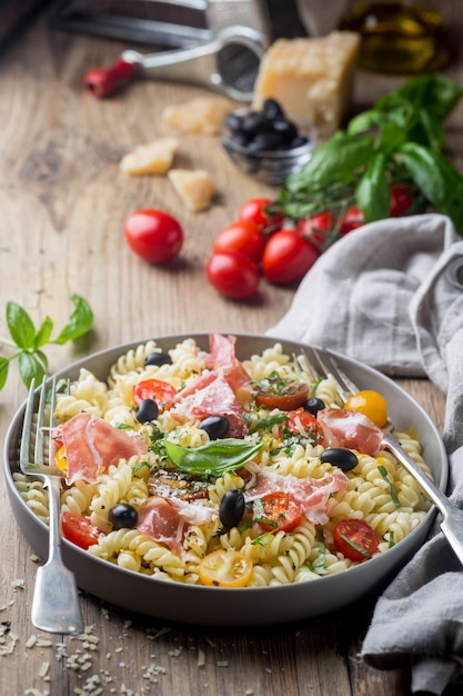 Italienische Fusilli-Spiralnudeln mit Traubentomaten, Oliven, Prosciutto und Parmigiano-Käse auf einem Teller