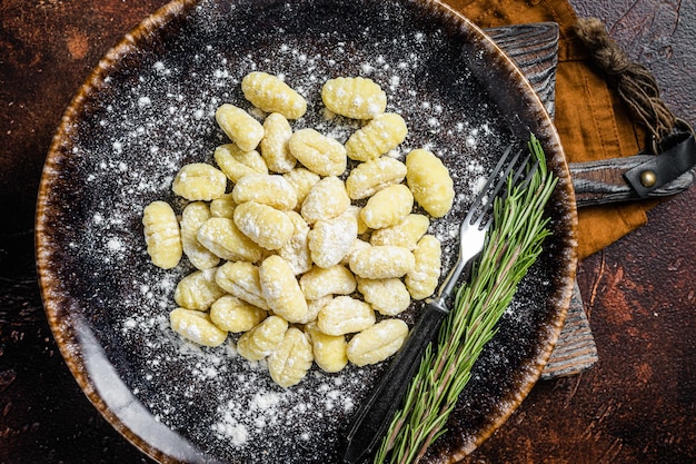 Italienische Gnocchiknödel, rohe Kartoffelgnocchi auf Teller mit Thymian. Dunkler Hintergrund. Ansicht von oben.
