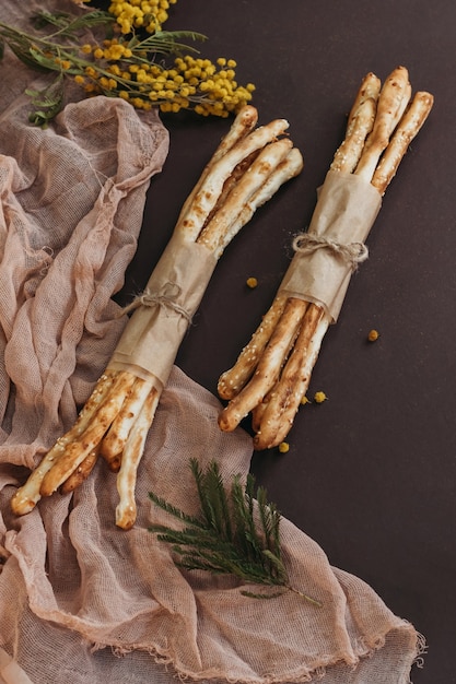 Italienische Grissini oder gesalzene Brotstangen auf braunem Hintergrund mit Blumen und beigefarbenem Tuch