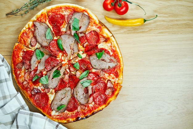 Italienische, hausgemachte Pizza mit Fleisch, Salami und Paprika auf einem Holztisch.