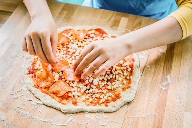 Italienische Küche. Frische leckere Pizzazubereitung. Weibliche Hände, die Peperoni auf Pizza setzen.