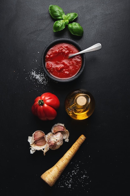 Italienische Lebensmittelzutaten mit Gemüse und Tomatensauce auf dunklem Tisch. Draufsicht.