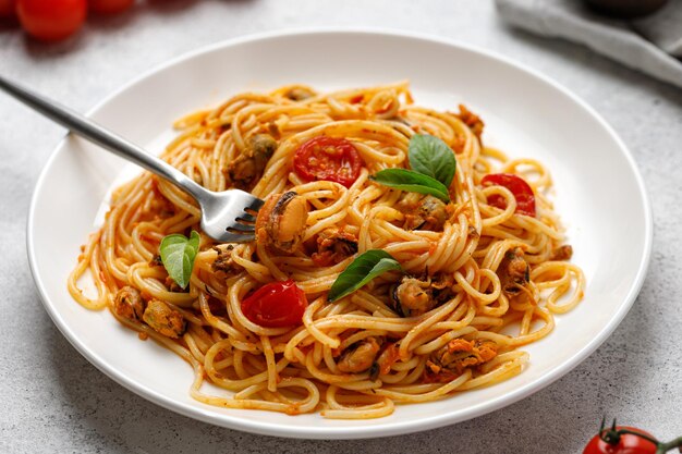 Italienische Meeresfrüchtenudeln mit Muschelkirschtomatensoße in weißer Tellergabel mit Muschel