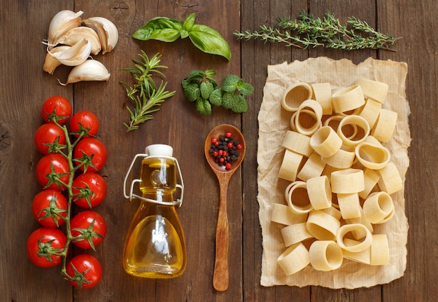 Italienische Nudeln, Gemüse, Kräuter und Olivenöl auf einem Holztisch, Draufsicht