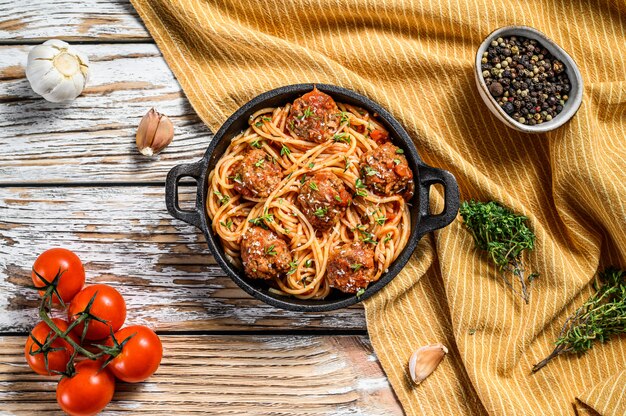 Italienische Nudelspaghetti mit Tomatensauce und Fleischbällchen in gusseiserner Pfanne mit Parmesan. Weißer hölzerner Hintergrund. Draufsicht