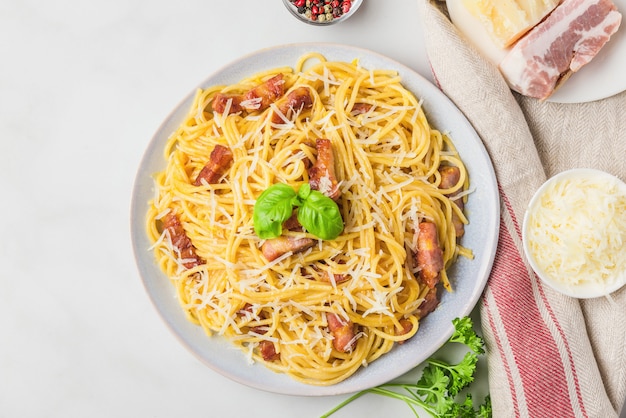 Italienische Pasta Carbonara aus Spaghetti, Speck, Parmesan und Basilikum in einem Teller auf weißem Marmortisch