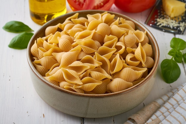 Italienische Pasta Conchiglie Rigate in einem Teller mit Basilikum Tomaten Olivenöl Pfeffer Parmesankäse auf weißem Hintergrund