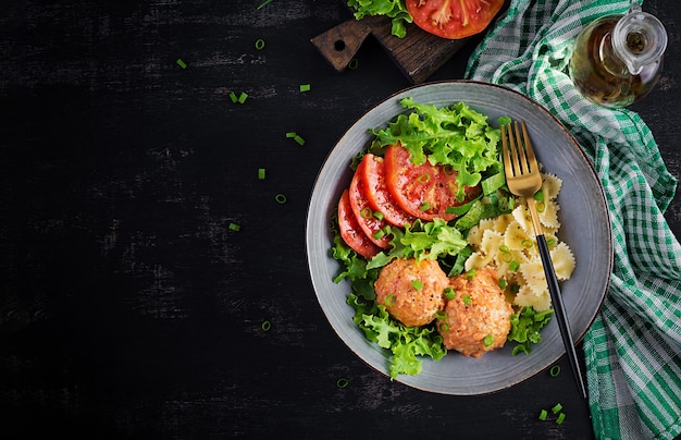 Italienische Pasta. Farfalle mit Fleischbällchen und Salat auf dunklem Tisch. Abendessen. Draufsicht, oben.