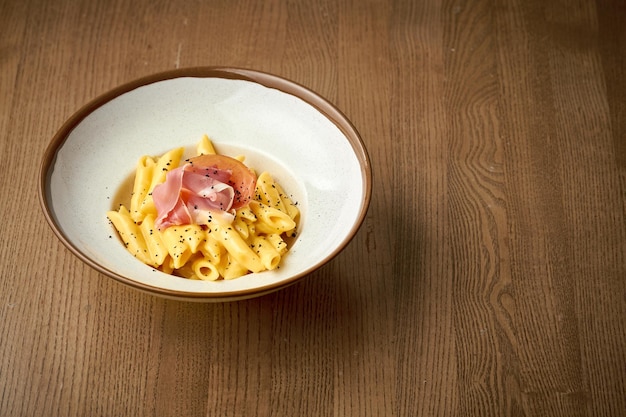 Italienische Pasta mit Käsesauce und Jamon in einem Teller auf Holzhintergrund