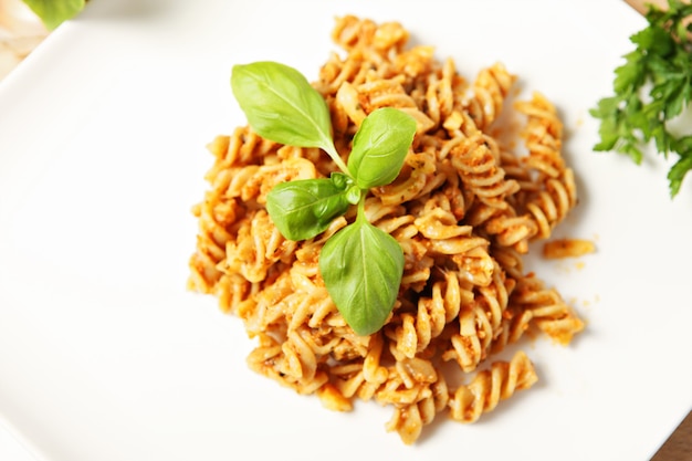 Italienische Pasta mit Paprika-Pesto auf einem weißen Teller serviert und mit Basilikum dekoriert