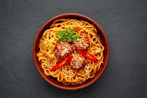 Italienische Pasta mit Tomatensauce und Fleischbällchen in einem Teller mit Gewürzen auf Stein