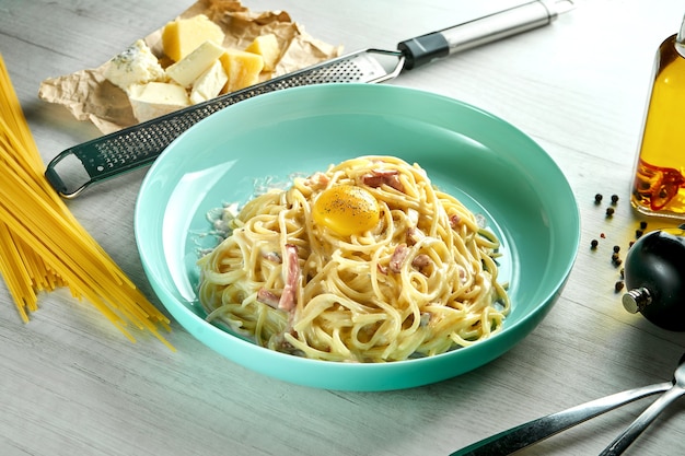 Italienische Pasta Spaghetti Carbonara mit Bechemalsauce, Speck und Eigelb, Parmesan, serviert in einem blauen Teller auf einem Holztisch. Restaurant Essen.