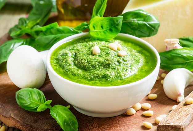 Italienische Pesto-Sauce in weißen Porzellanschüssel-Zutaten zum Kochen von selektivem Fokus auf Vintage-Holzhintergrund